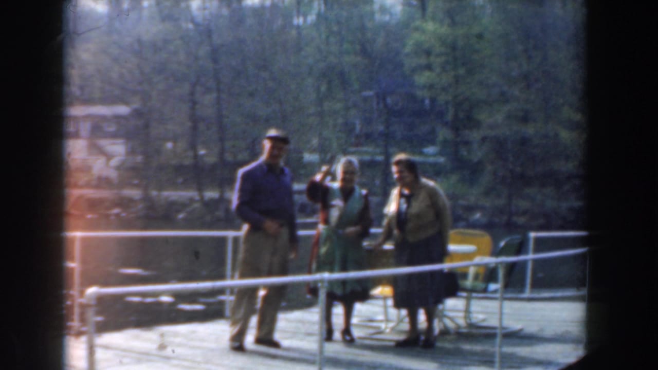 Adults stand on a dock as one woman holds up a fish near the water.