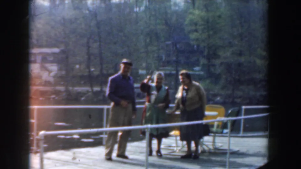 A 1961 Novi, Michigan dock scene shows three adults by the lake, with one woman appearing to hold up a fish for the home-movie camera.