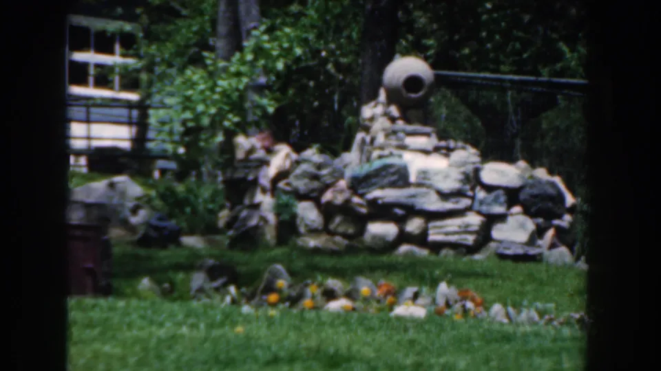 1961 Novi, Michigan home-movie frame with stone garden features, lawn, shrubs, and a round ceramic pot-like object.