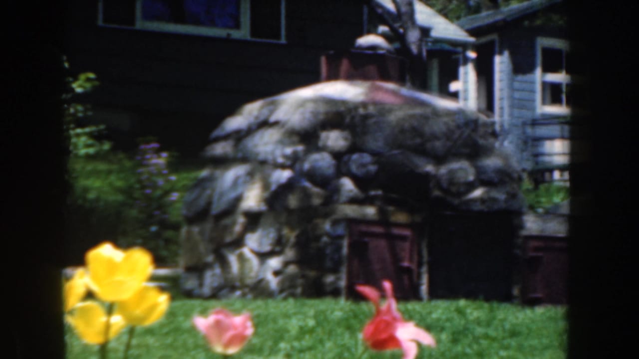 Yellow and pink tulips in front of a stone garden structure and house siding.