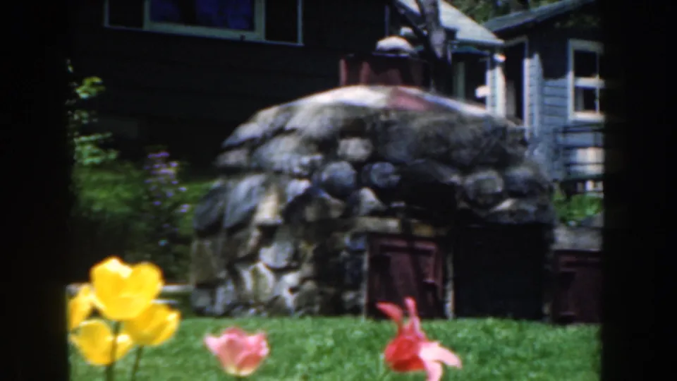 1961 Novi, Michigan frame with tulips in the foreground, a stone yard feature, small wooden doors, and residential siding behind.