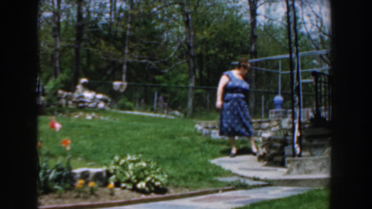 Woman in a blue dress near a curved path and stone wall in a backyard.