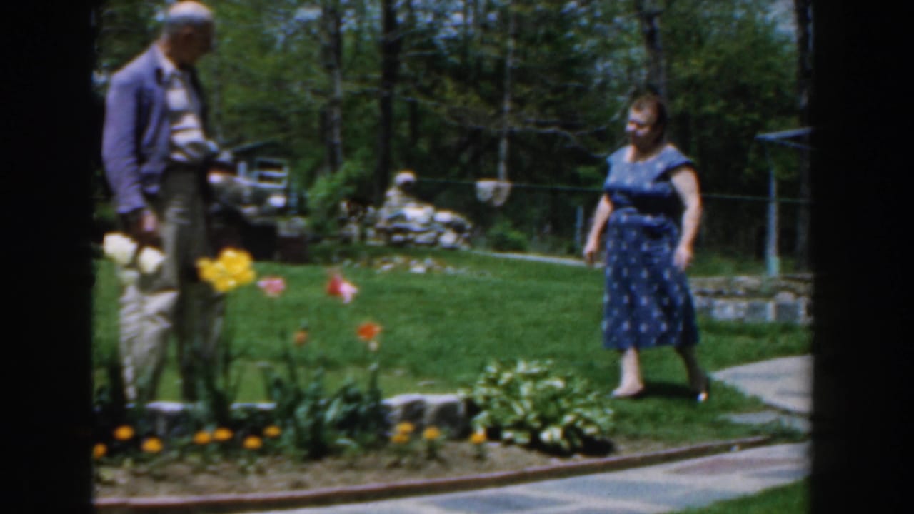 Man and woman standing near tulips and a curved backyard walkway.