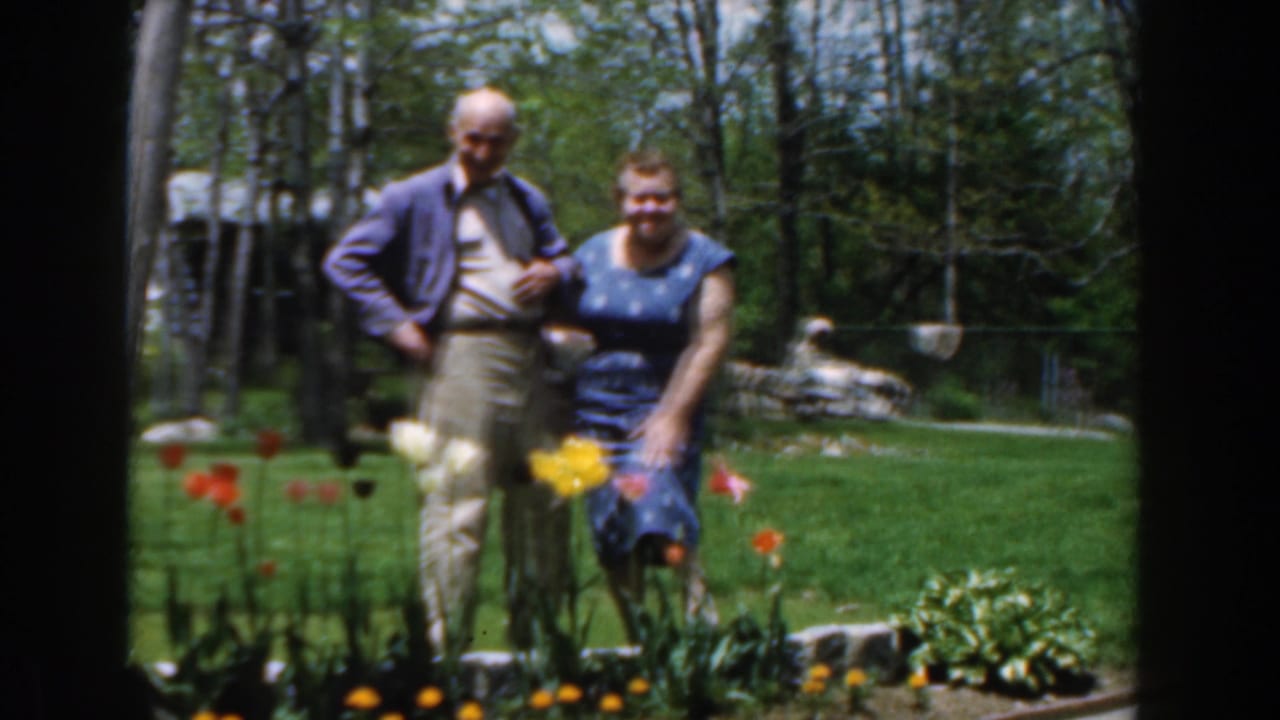 Elderly couple standing beside tulips in a backyard garden.