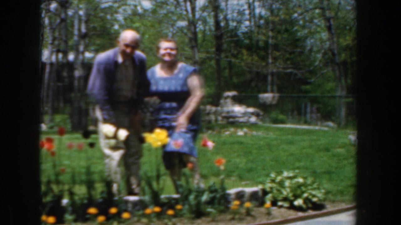 Smiling elderly couple posed behind tulips in a green yard.