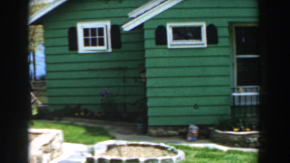 1961 Novi, Michigan 8mm frame showing a green-sided house with white trim, black shutters, grass, and stone-edged landscaping.