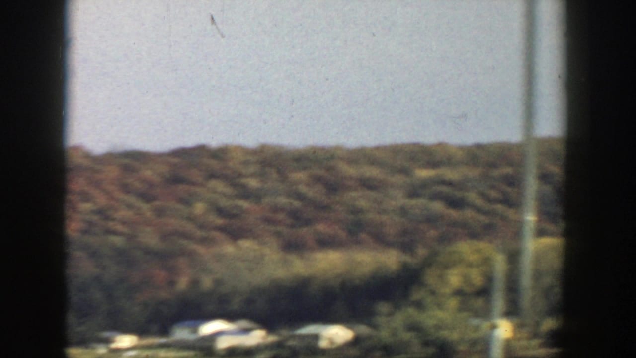 Distant cabins and tree-covered hillside framed by dark vertical bars.