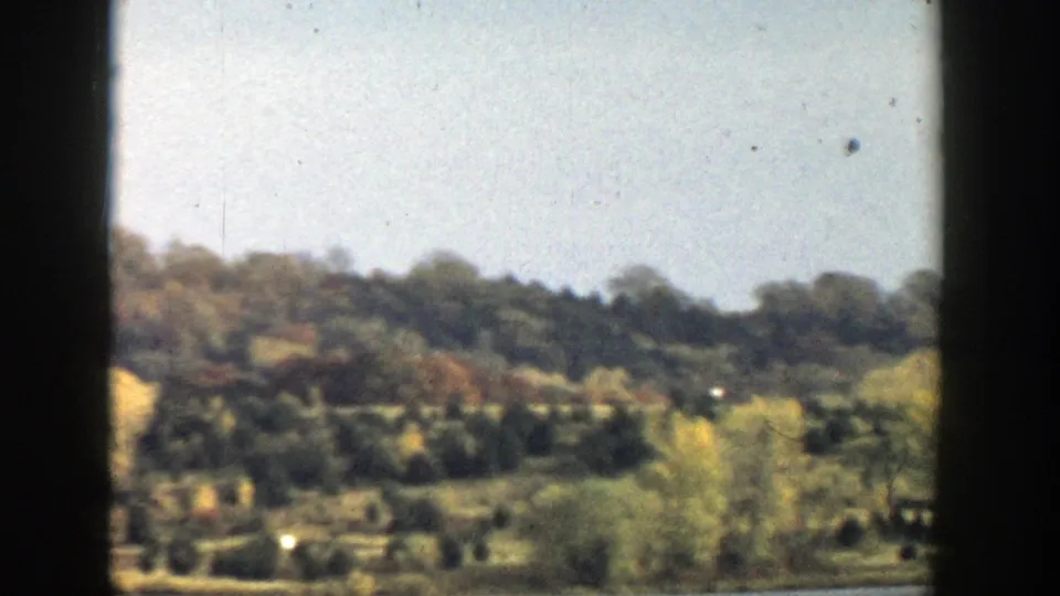 Wisconsin lakeside hillside with dense trees and shore vegetation, recorded in soft 8mm color through a dark frame.