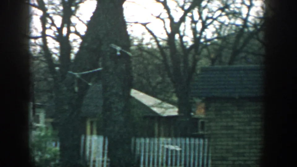 1957 Wisconsin home-movie view of leafless trees, a white picket fence, small buildings, and a trailer-park exterior.