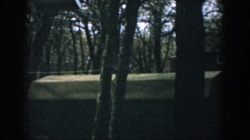 1957 Wisconsin 8mm frame showing a wooded residential yard with a house partly visible through trees.