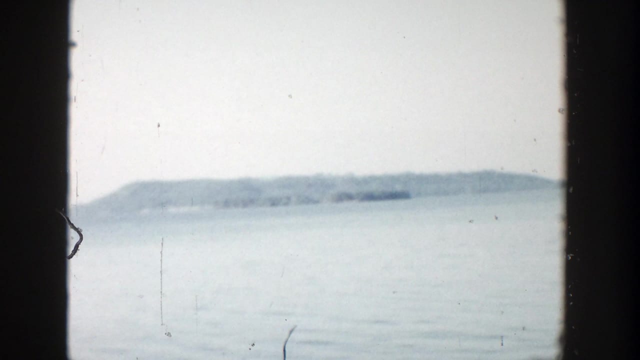 Soft lake view with a distant low shoreline under a pale sky, framed by dark film borders.