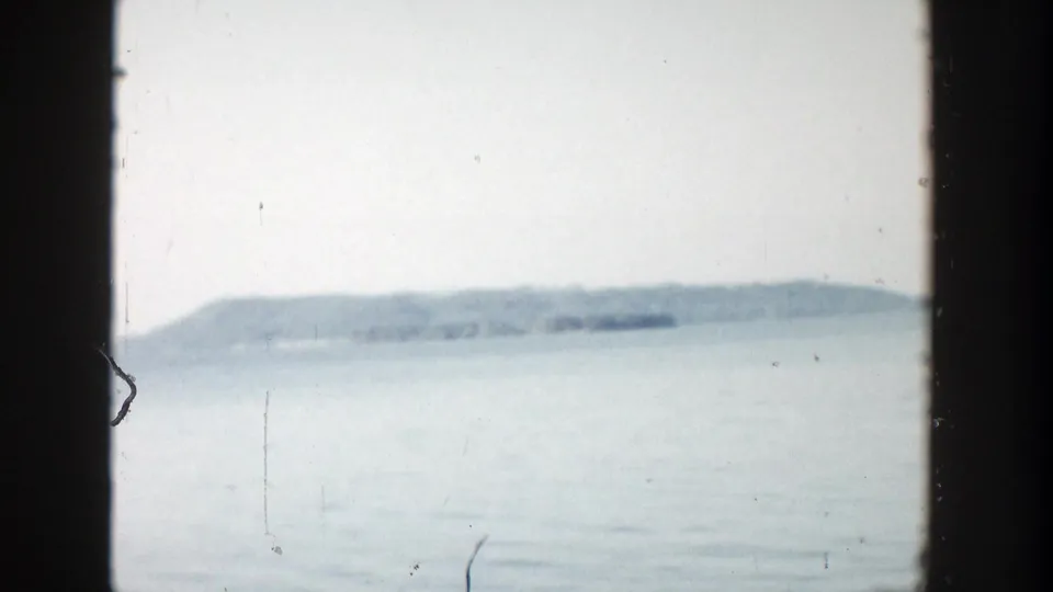 1957 Wisconsin 8mm frame showing open water and a hazy tree-lined shore in soft blue-gray tones.