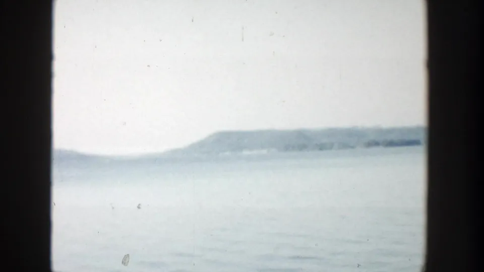 1957 Wisconsin home-movie frame with calm water, a soft horizon, and a distant wooded hill.