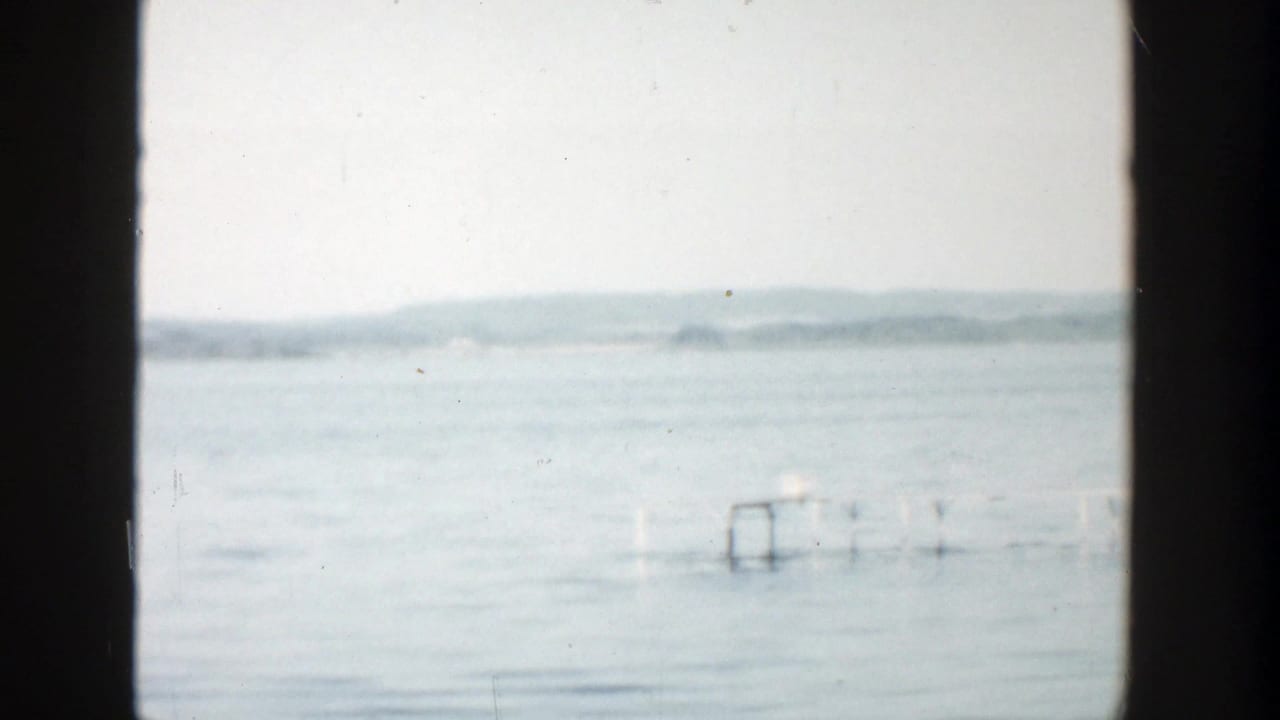 Open lake with distant shore, pale sky, and a small dock-like structure at right.