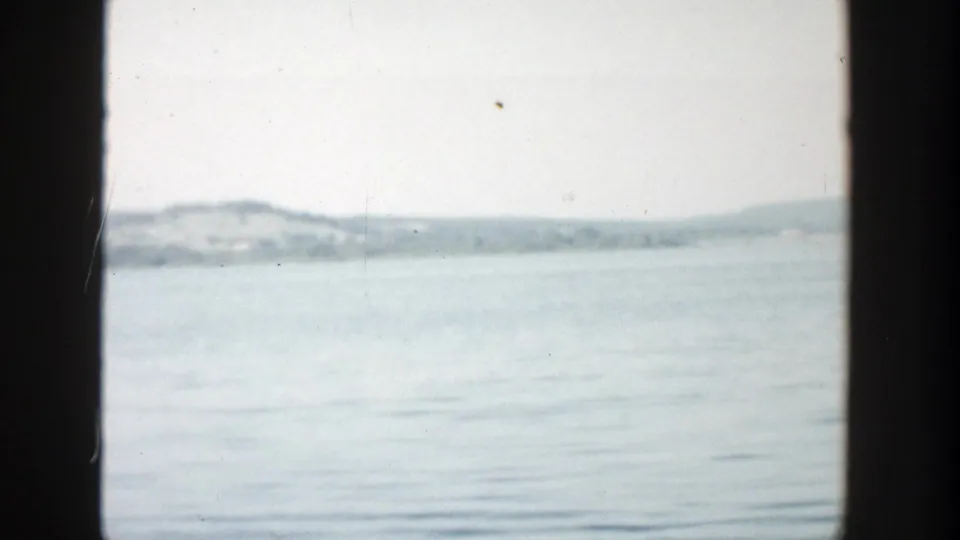 1957 Wisconsin lake scene showing calm rippled water, a distant wooded shore, pale sky, and a dark vertical border at left.