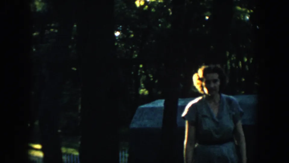 1957 Wisconsin home-movie frame with the woman closer to the lens, her face partly lit against a dark wooded background.