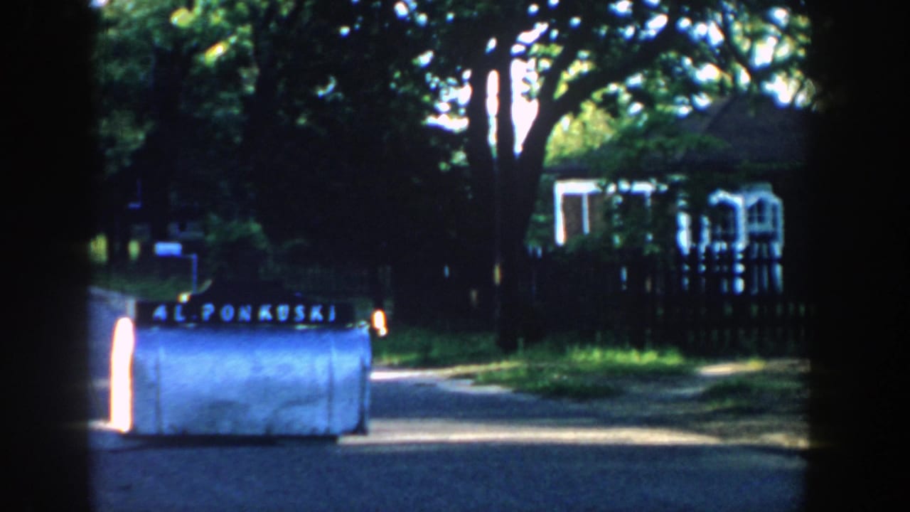 Roadside mailbox marked 42 PONKUSKI beside a quiet street and house.