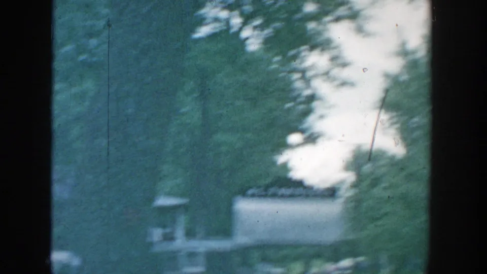 1957 Wisconsin 8mm frame looking through dark window divisions toward trees and a pale building beyond a shaded lawn.