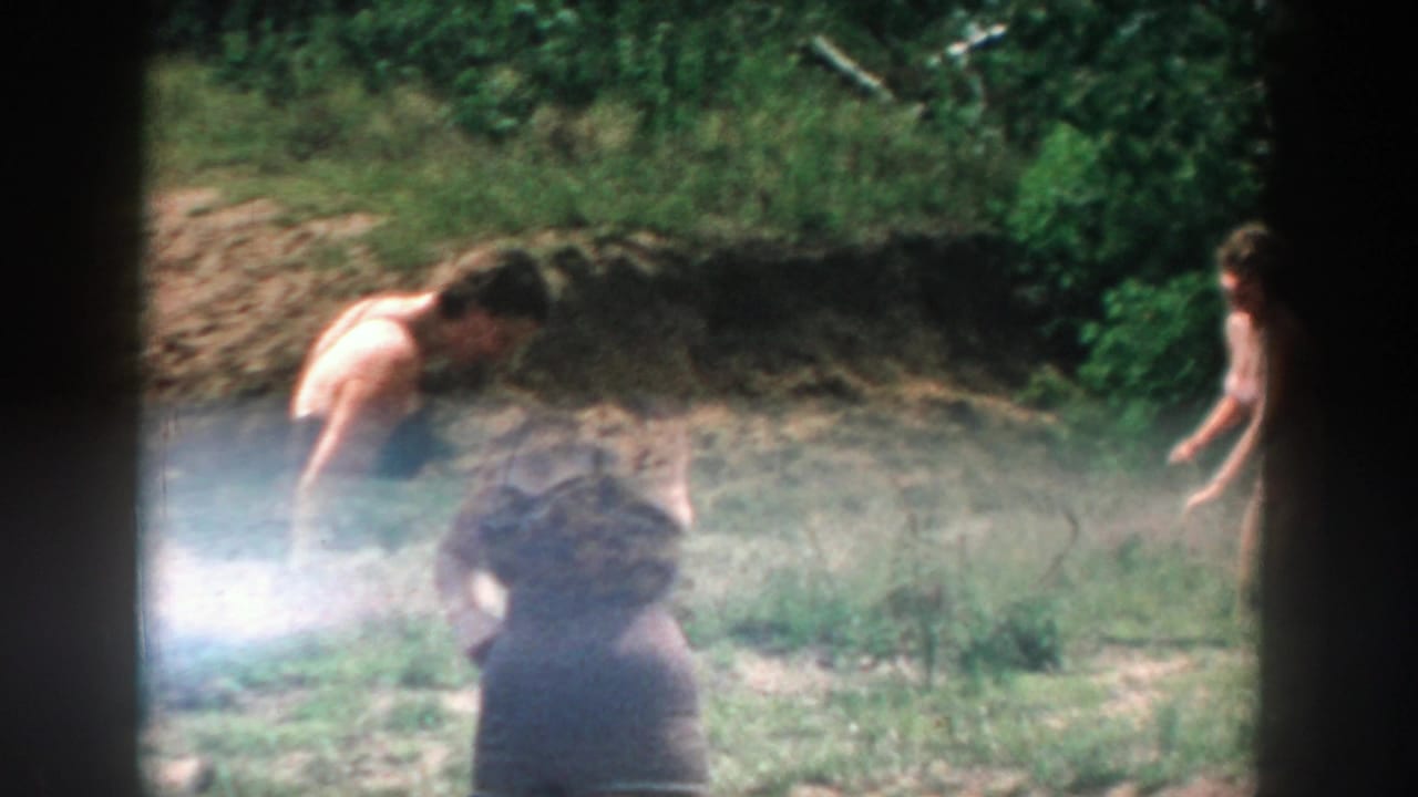 Two adults near a grassy bank, with one figure partly obscured by glare and film edge.