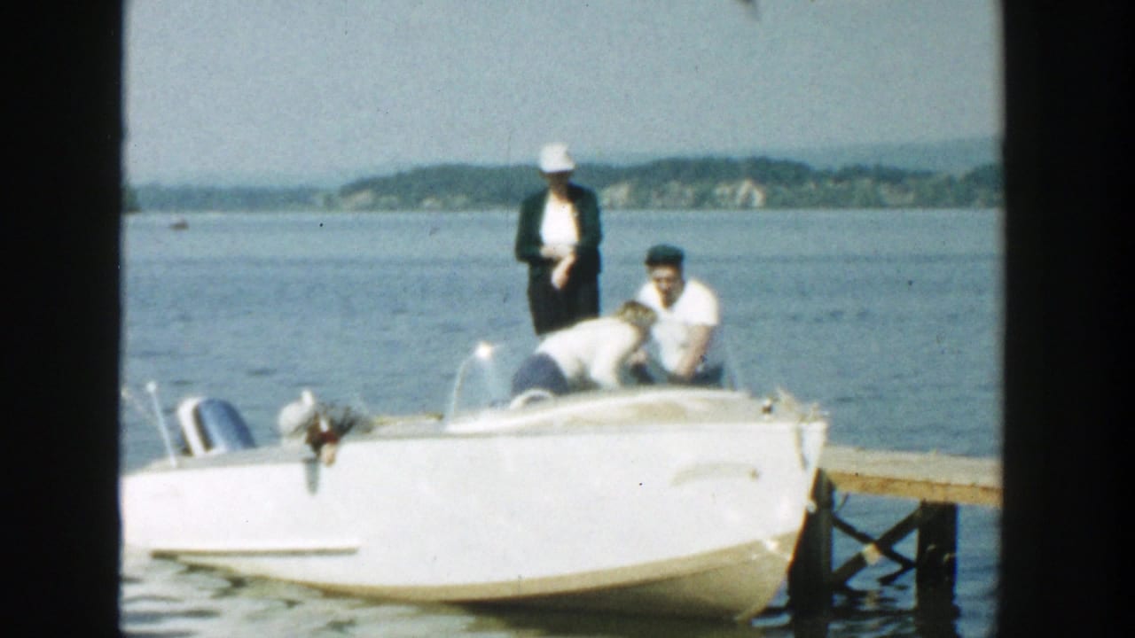 Family members gathered around a white motorboat beside a wooden dock on a lake.