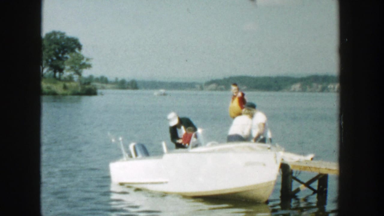 Small white motorboat beside a dock on a lake with several people aboard.