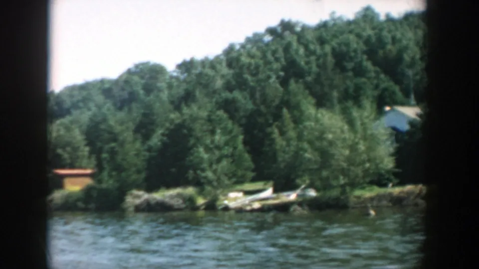 Soft 8mm view of a Wisconsin lake shore with moored boats, dense trees, and small buildings glimpsed through greenery.