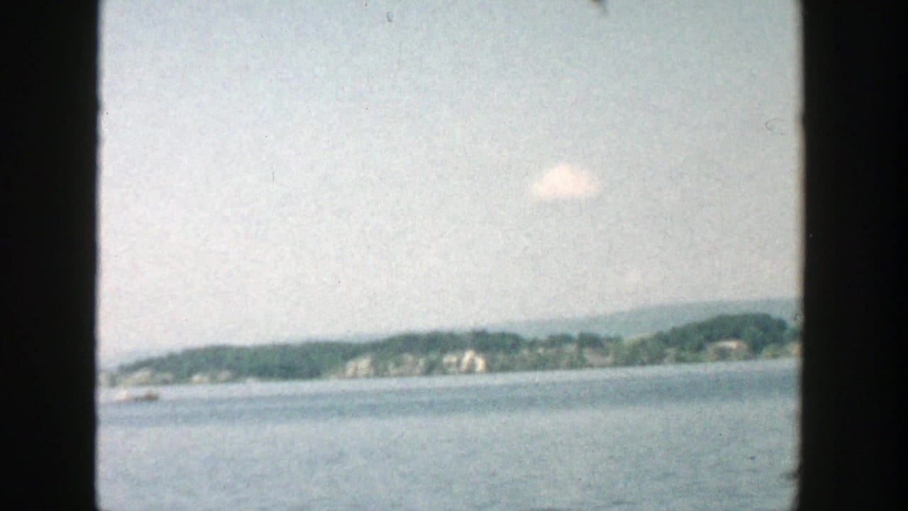 Open lake with a distant wooded shore, pale sky, and dark vertical frame edges.