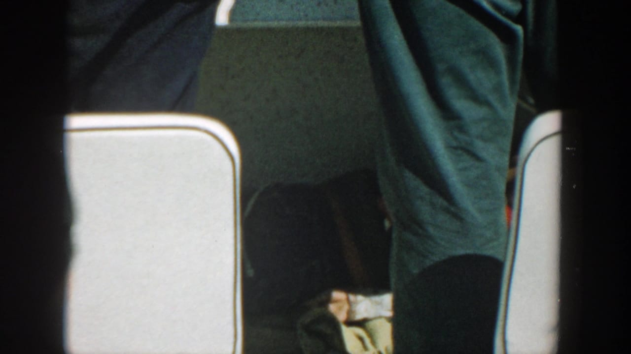 Dark trousered adults stand near white seating in a boat.