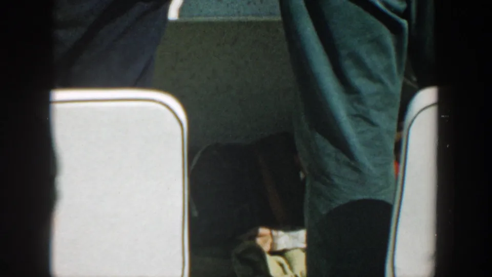 Adults in dark trousers stand close to white-trimmed seats inside a boat, with faces outside the frame.
