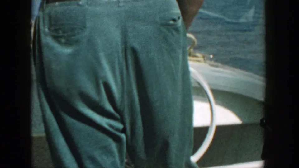 A standing adult in dark trousers is seen beside white boat trim, with water visible outside the boat.
