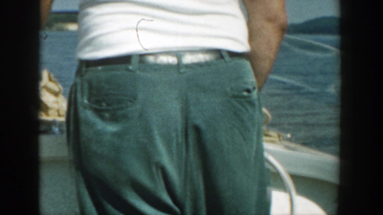 1957 Wisconsin 8mm frame showing an adult from behind on a boat, with water, shoreline, and sky partly visible beyond the deck.