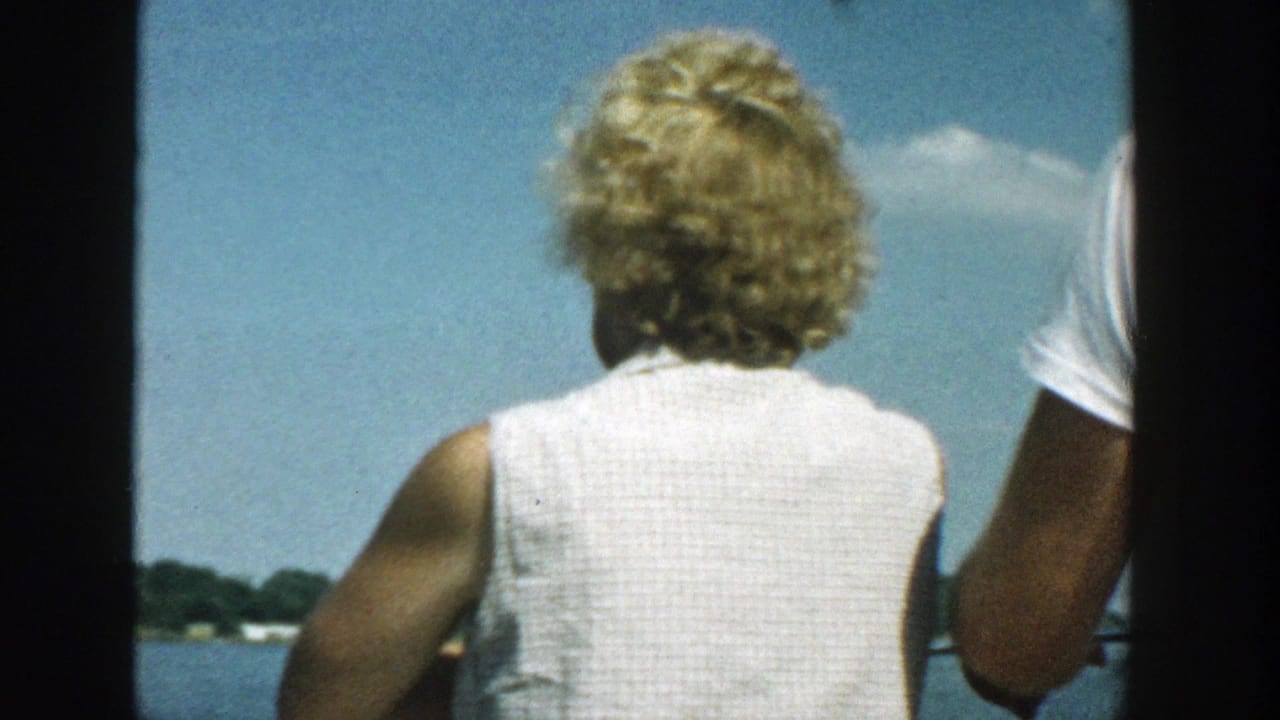 Blonde woman seen from behind on a boat facing a lake and distant shore.