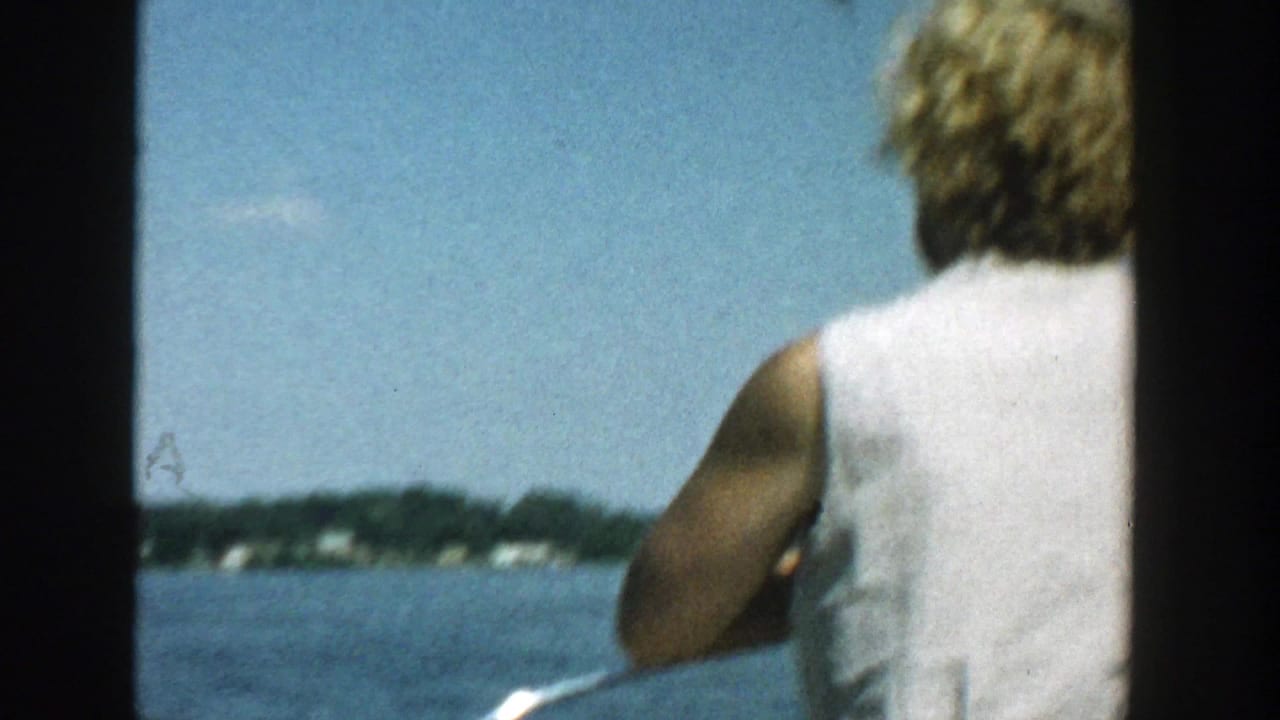 Woman and partial man viewed from behind on a boat with lake and shoreline ahead.