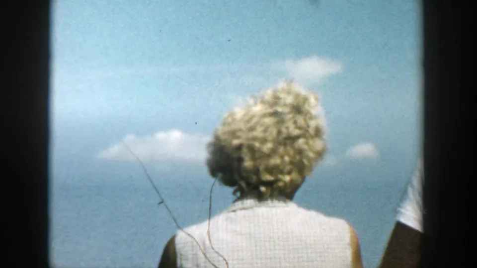 1957 Wisconsin 8mm frame with the back of a blonde woman in a sleeveless top under a bright sky on a lake boat.