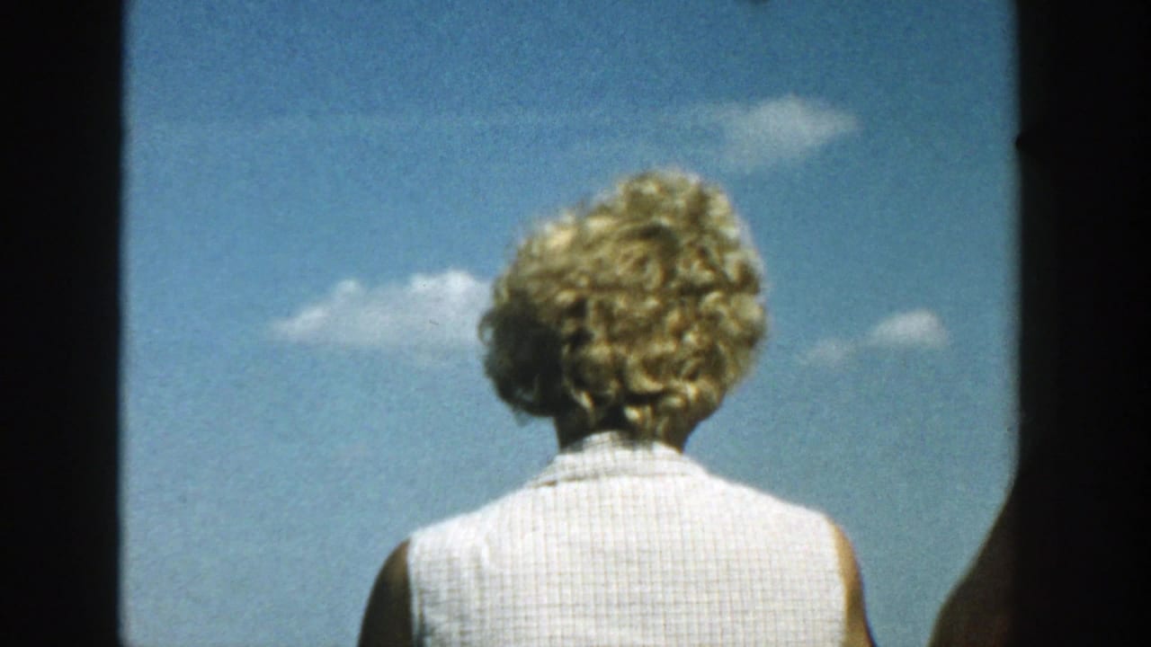 Woman with curly blonde hair seen from behind against a blue sky.