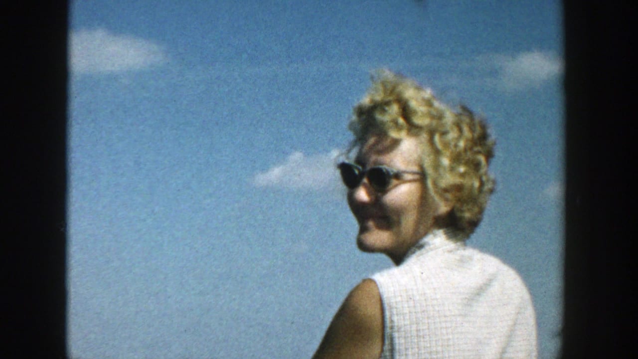 Woman in sunglasses turns and smiles against a blue sky.