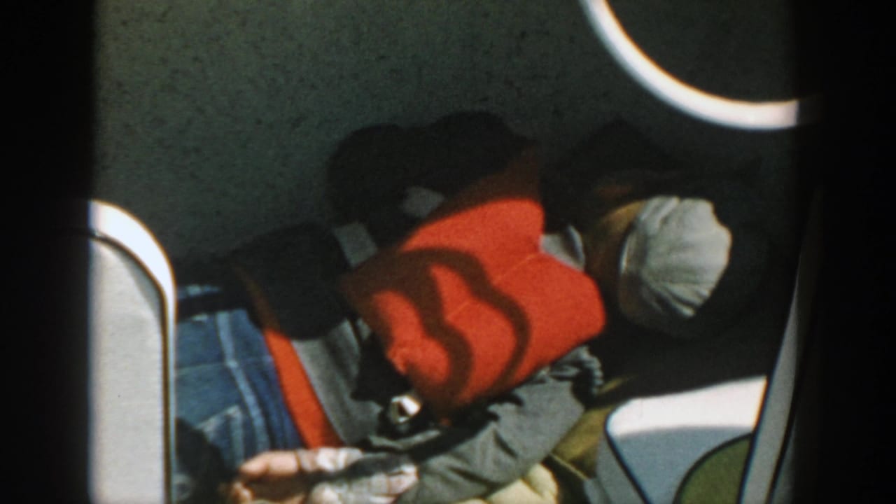 Person rests below deck with a red life jacket, white cap, denim, and boat railing nearby.
