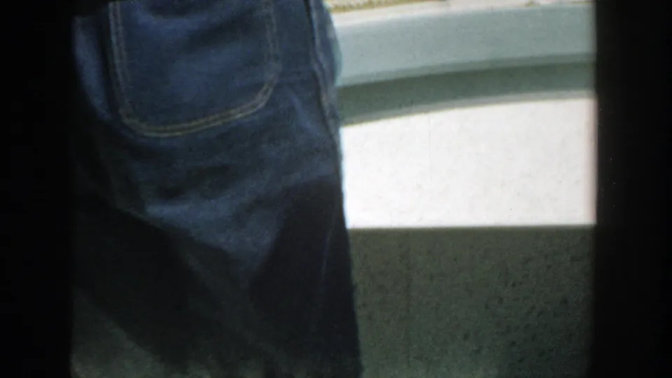 1957 Wisconsin 8mm frame with a close view of denim clothing on a boat, white hull or seating surface, and shadowed below-deck space.