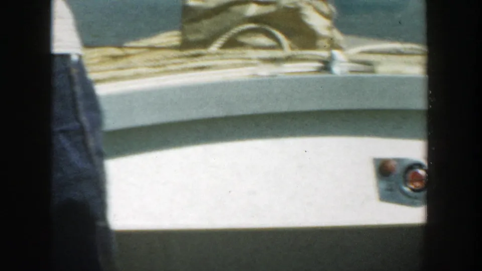 Close view of denim-clad legs near the white deck of a boat in 1957 Wisconsin home-movie footage.