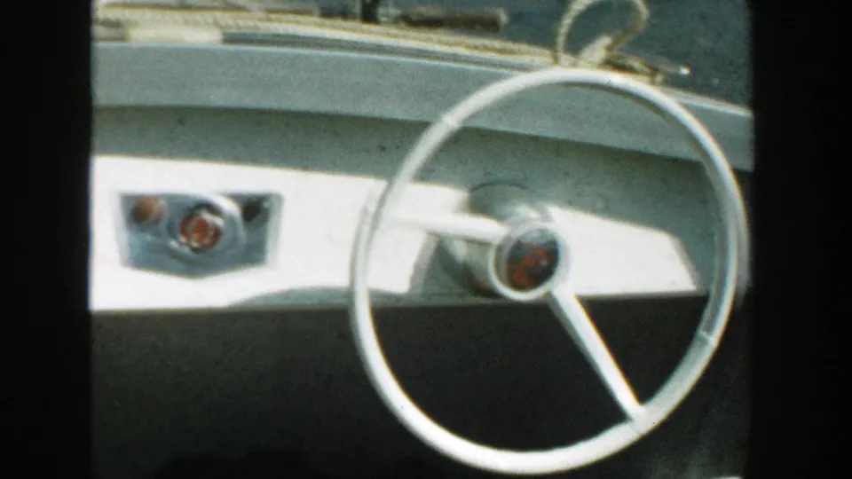White speedboat dashboard with a round steering wheel and simple controls, seen in 1957 Wisconsin footage.