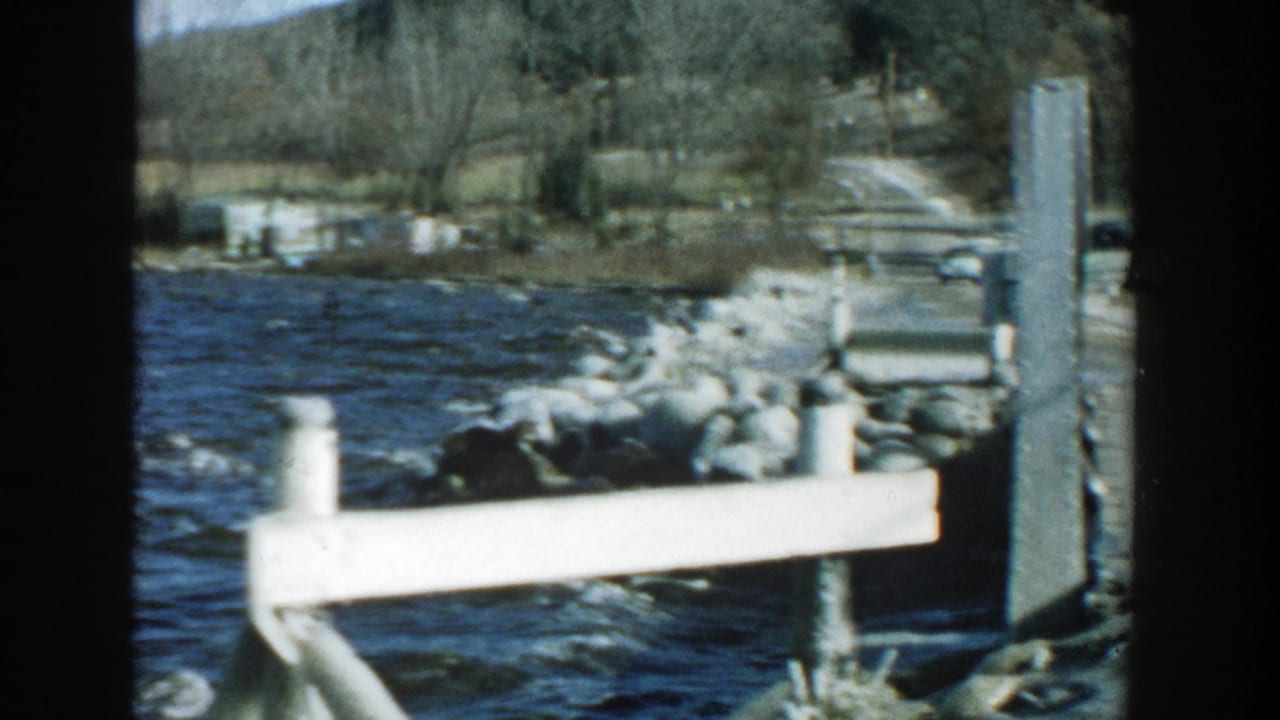 White dock rail beside choppy lake water with rocks and shoreline beyond.