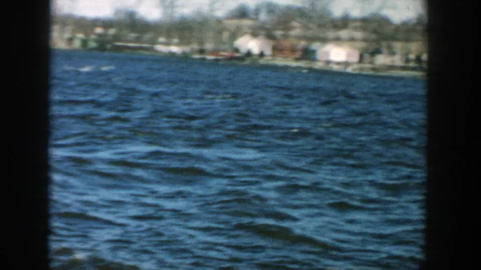 Wide 1957 Wisconsin lake view with wind-ruffled water, distant houses, bare trees, and soft home-movie color.