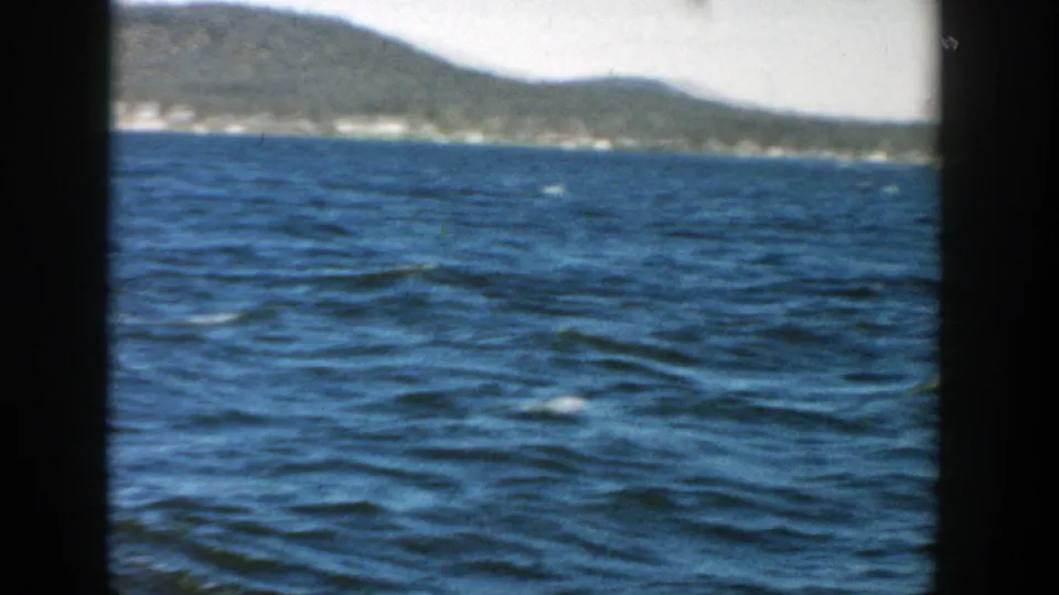 1957 Wisconsin 8mm frame showing open lake water, a wooded hill, and a soft distant shoreline.