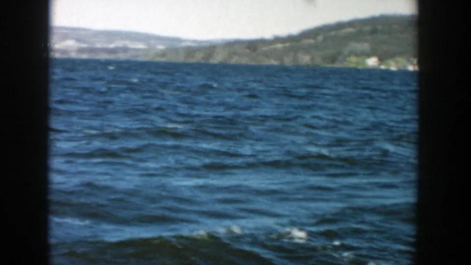 1957 Wisconsin home-movie frame with choppy lake water, distant wooded hills, and bright sky.