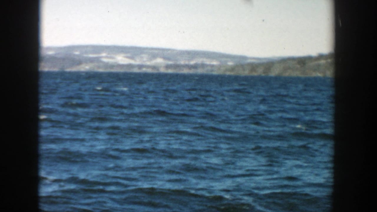 Choppy blue lake water with distant low shoreline and dark film frame edges.