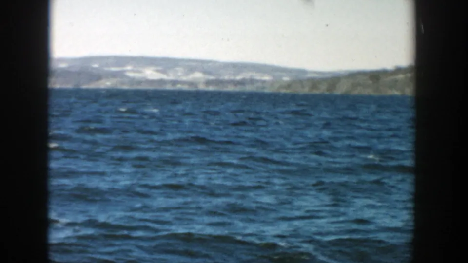 1957 Wisconsin 8mm frame showing wind-ruffled lake water and a low distant shoreline under a pale sky.