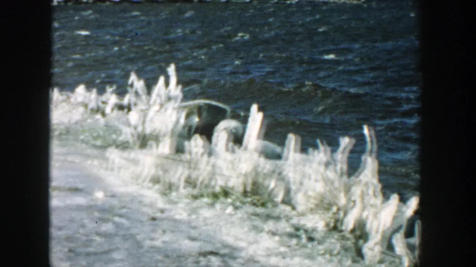 1957 Wisconsin 8mm frame focused on jagged ice along a winter riverbank with rippling water in the background.
