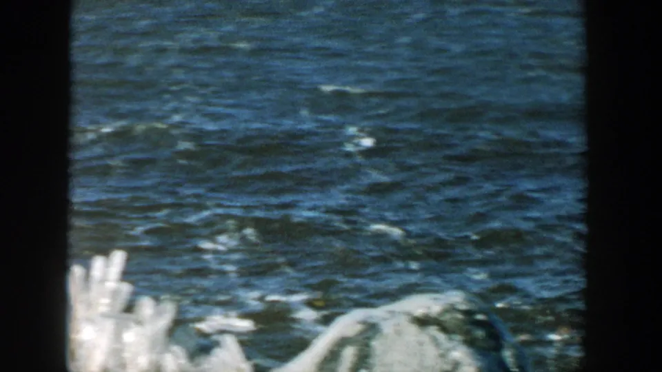 Close 8mm view of choppy blue river water and pale shore ice in a 1957 Wisconsin riverside home movie.