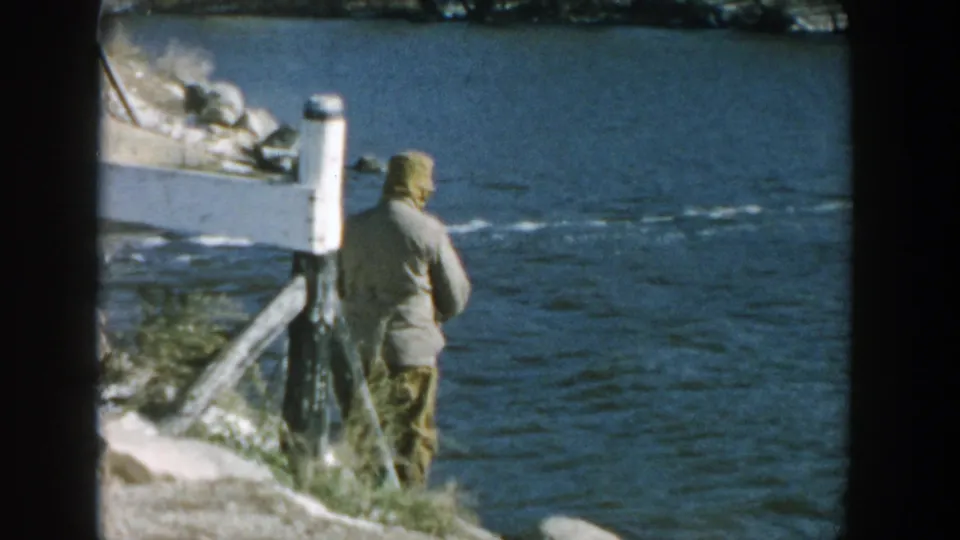 The fisherman stands with his back to the camera on a Wisconsin riverbank, holding a rod toward the water.