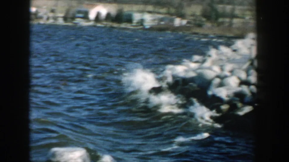 A larger wave strikes the Wisconsin breakwater, sending white spray over the rocks in a 1957 home-movie view.